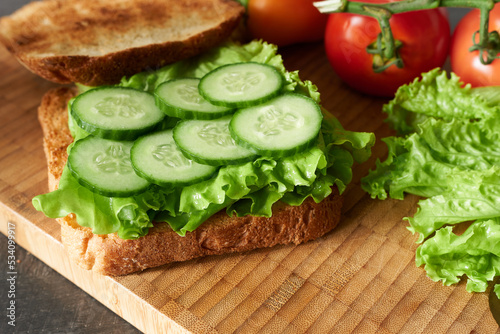 Sandwich with lettuce leaves and cucumber on a wooden background. The concept is a meal for a vegetarian.