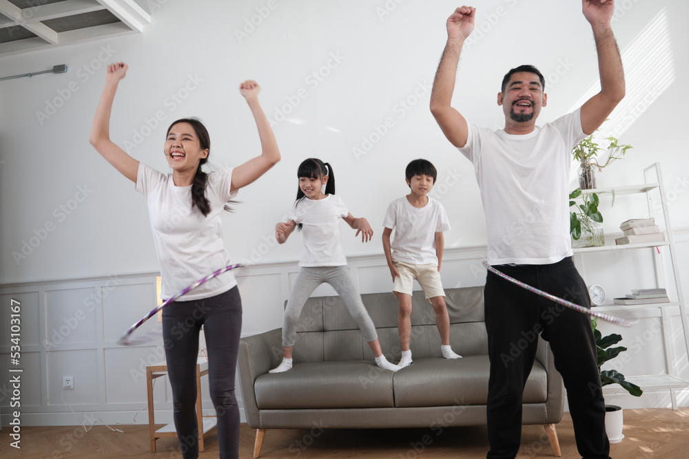 Happy wellness Asian Thai family, parents, and children are fun playing hula hoops together, fitness training and healthy exercise in white living room, domestic home lifestyle, and weekend activity. Happy wellness Asian Thai family, parents, and children are fun playing hula hoops together, fitness training and healthy exercise in white living room, domestic home lifestyle, and weekend activity.