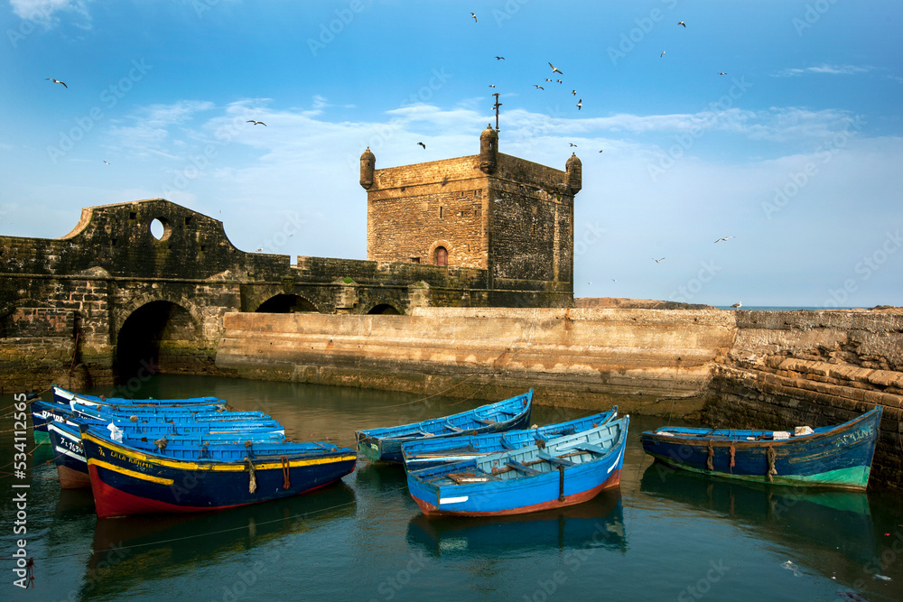 Fishing boats docked in the port Skala fort at Essaouira in Morocco. The Genoese-built citadel stands in the background adjacent to the Atlantic Ocean.