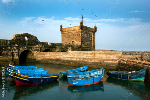 Fishing boats docked in the port Skala fort at Essaouira in Morocco. The Genoese-built citadel stands in the background adjacent to the Atlantic Ocean.