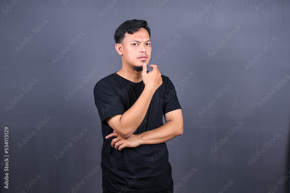 Asian young man thinking about things or idea wearing black t-shirt. Isolated gray background