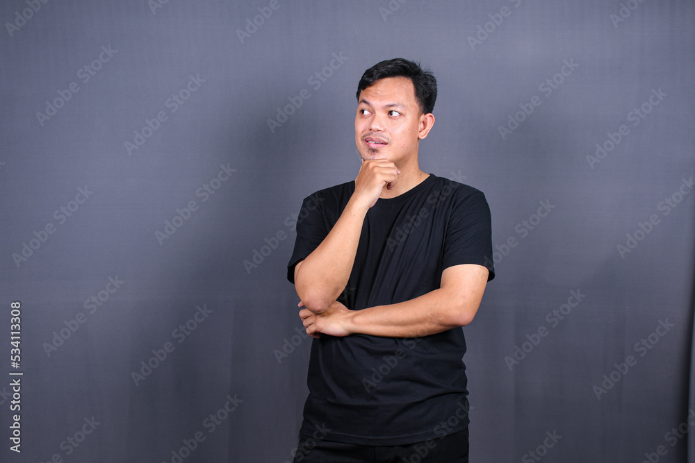 Asian young man thinking about things or idea wearing black t-shirt. Isolated gray background Asian young man thinking about things or idea wearing black t-shirt. Isolated gray background