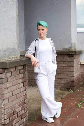 A woman with green hair in white clothes and with an umbrella walks down the street after the rain