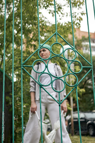 A woman with green hair in white clothes and with an umbrella walks down the street after the rain