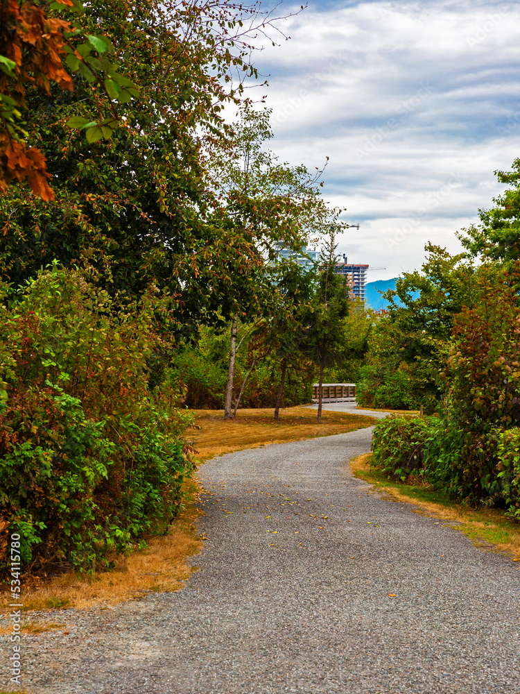Walkway on the Brunet-Fraser Regional Greenway On the Fraser River waterfront and flower beds green trees and shrubs in autumn time in New Westminster City