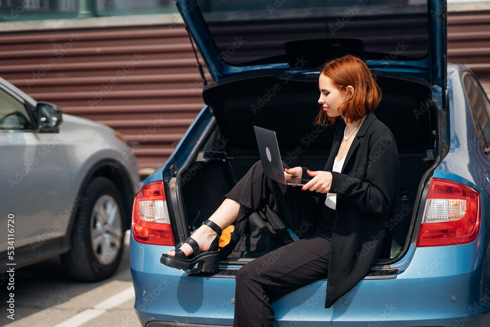 Woman working on laptop while sitting in trunk of car Woman working on laptop while sitting in trunk of car