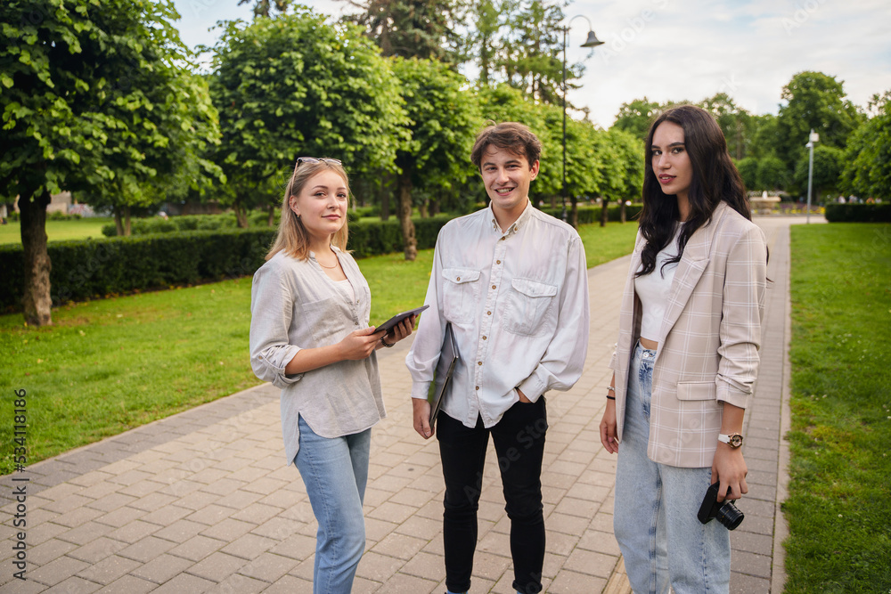 Shot of three students with laptop and tablet walking in park of city in summertime. Shot of three students with laptop and tablet walking in park of city in summertime.