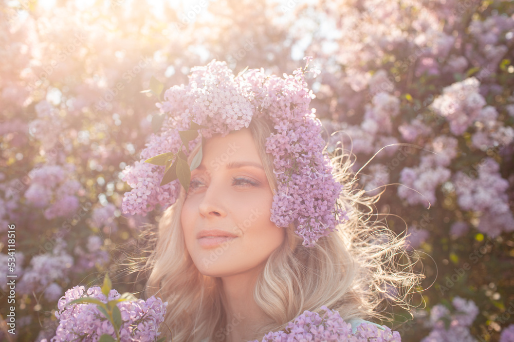 Portrait of a beautiful girl with a wreath on her head made of a purple flowers. A woman walks outside against the background of flowering purple trees Portrait of a beautiful girl with a wreath on her head made of a purple flowers. A woman walks outside against the background of flowering purple trees