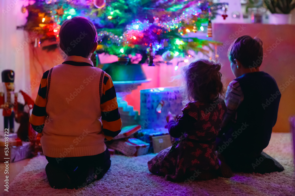 Two little kid boys and adorable toddler sitting by Christmas tree with old vintage toys and balls with lots of present on Xmas eve. Family preaparation celebration of family feast