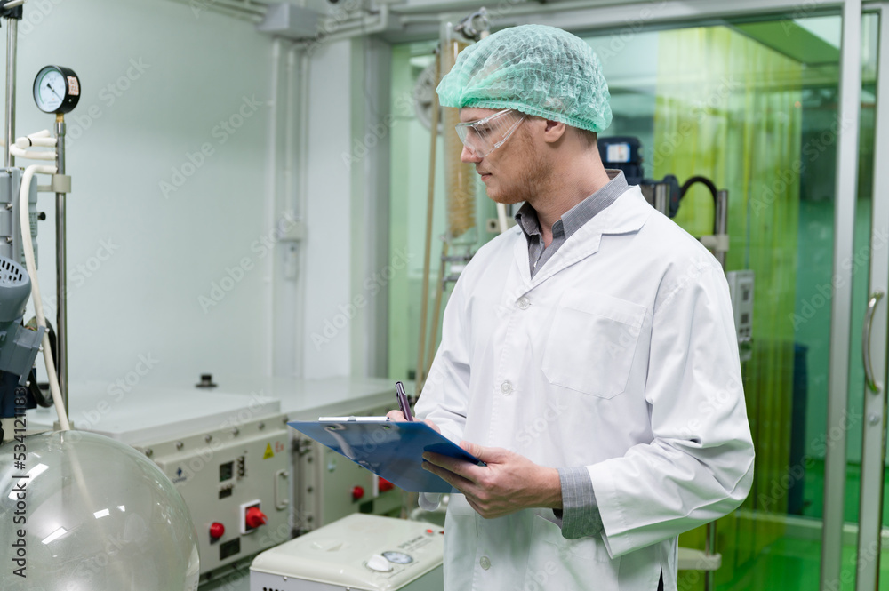 Inspector caucasian scientists use clipboard in the machine room extracting oil and cannabis seeds Inspector caucasian scientists use clipboard in the machine room extracting oil and cannabis seeds