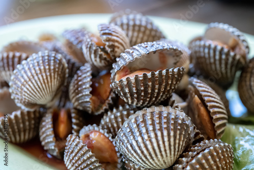 Steamed cockle or Boiled cockles on the dish with spicy seafood sauce and vegetable in restaurante wooden background