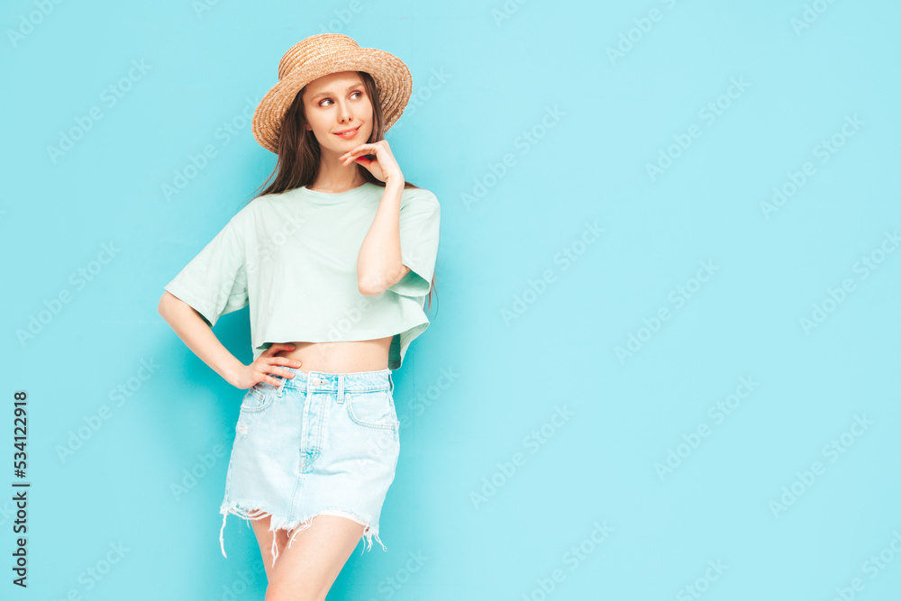 Portrait of young beautiful smiling female in trendy summer jeans skirt. carefree woman posing near blue wall in studio. Positive model having fun indoors. Cheerful and happy. In hat Portrait of young beautiful smiling female in trendy summer jeans skirt. carefree woman posing near blue wall in studio. Positive model having fun indoors. Cheerful and happy. In hat