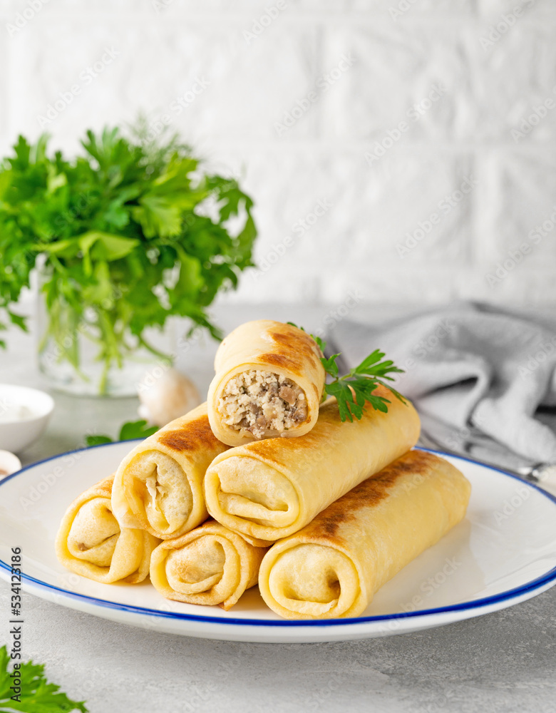 Pancakes or thin crepes stuffed with chicken and mushrooms on a plate on a gray concrete background. Selective focus, copy space.