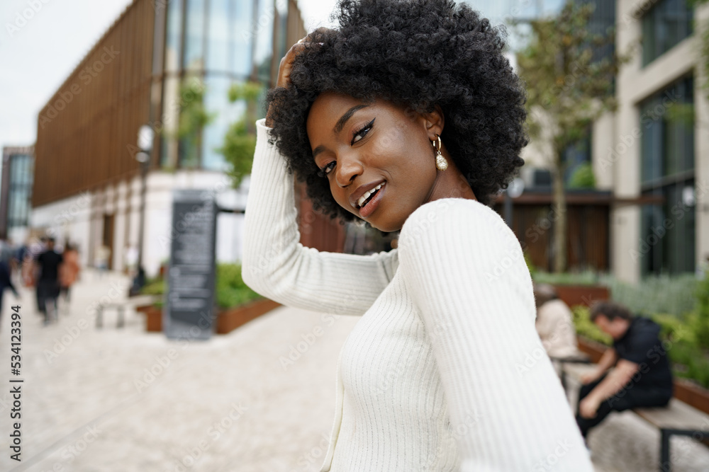 Fototapeta premium Portrait of young african woman with afro hairstyle smiling in urban background