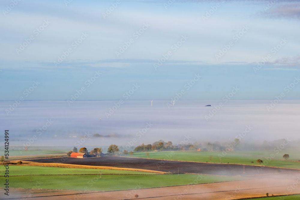Fototapeta premium View at farm in the countryside with fog on the fields