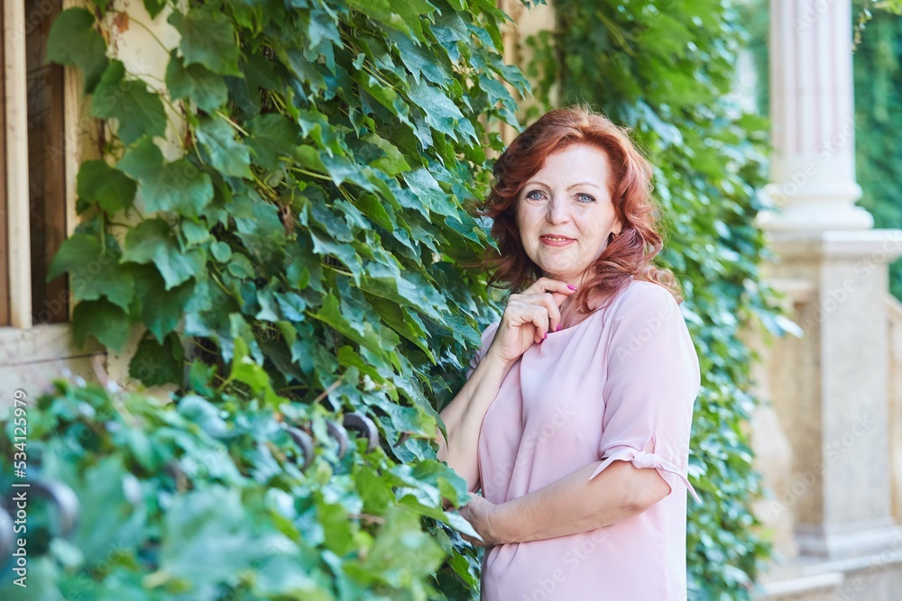 Portrait of a beautiful red-haired mature woman in a pink dress on the street. Portrait of a beautiful red-haired mature woman in a pink dress on the street.
