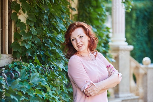 Portrait of a beautiful red-haired mature woman in a pink dress on the street.