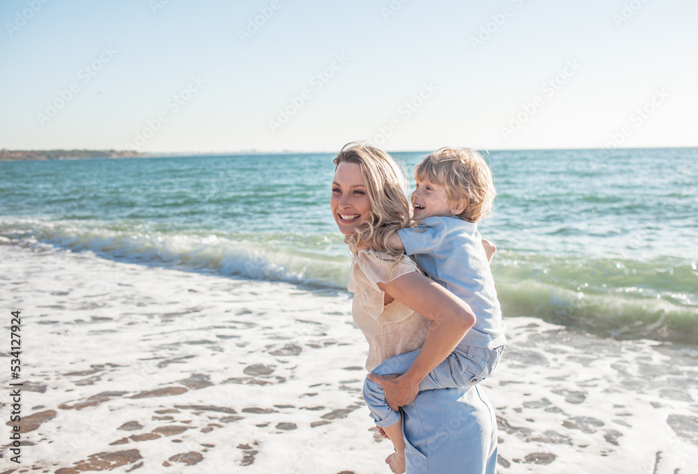 Mom and son are walking on the beacj, the woman hugs and kisses the child in her arms. people together. Mom and son are walking on the beacj, the woman hugs and kisses the child in her arms. people together.
