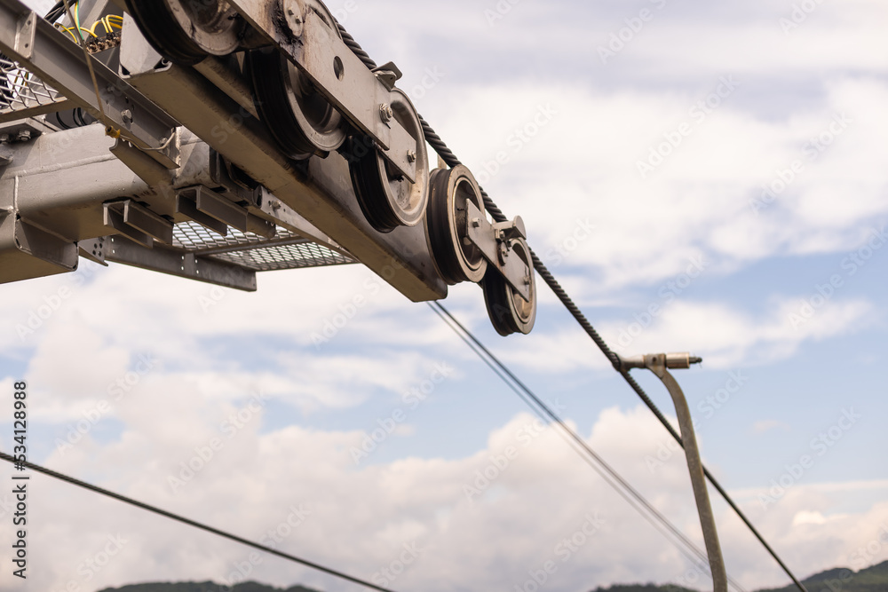 powerful metal wheel in a strong reliable mechanism on a mountain comfortable multi-colored lift in a mountain spruce and deciduous forest, against a cloudy sky.