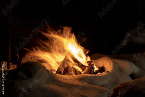 Campfire burns in the snow in the woods.. campfire burning in cold winter. Snow, forest and fire. Winter. Tourism. Flames on snow. Winter background. Nature