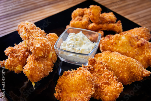 Breaded chicken fillet and king prawns with creamy sauce on a black plate photo