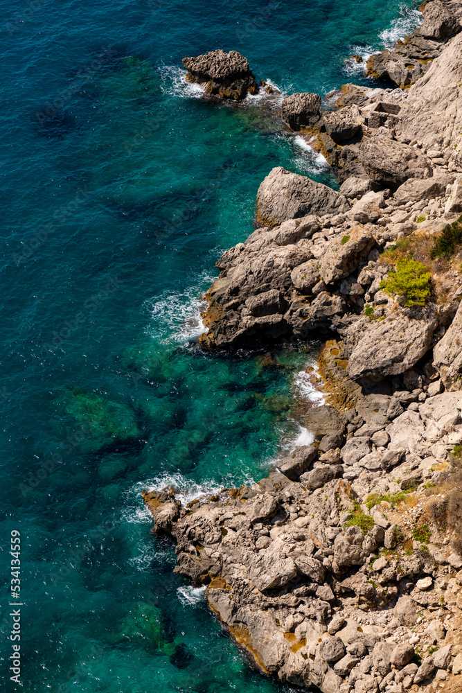 Rocky limestone cliffs and rocky shore of Capri island in Italy surrounded by deep blue and turquoise mediterranean sea in Gulf of Naples. View point near “Marina piccola“ harbour and Capri village.