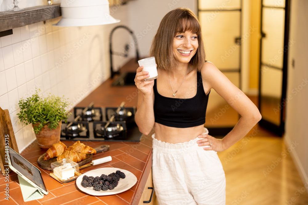 Portrait of young and cheerful woman whiich drinks dairy beverage during a breakfast time on kitchen of modern apartment. Wellness and domestic lifestyle concept
