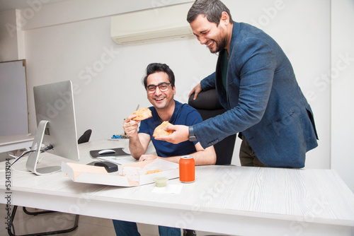 Work colleagues laughing as they share a slice of pizza at work.