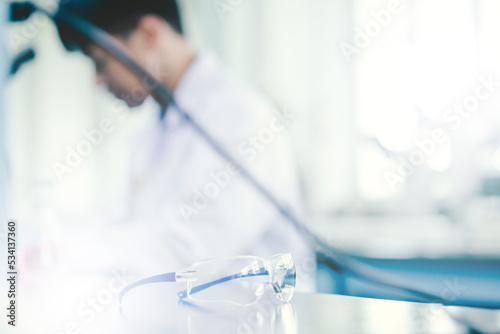 Medical Research Laboratory:Safety glasses with blurred Asian Male Scientist background and warm sunlight