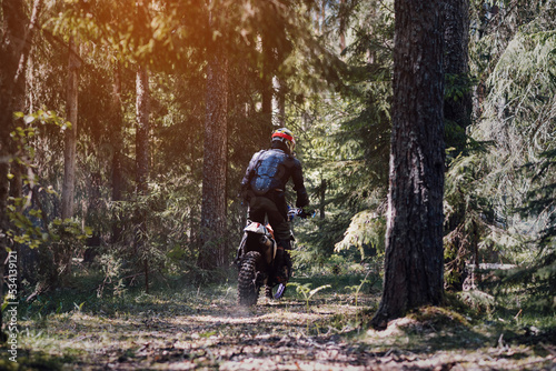 motorcycle racer on an enduro sports motorcycle rides through the forest in an off-road race in summer on a sunny day from the back