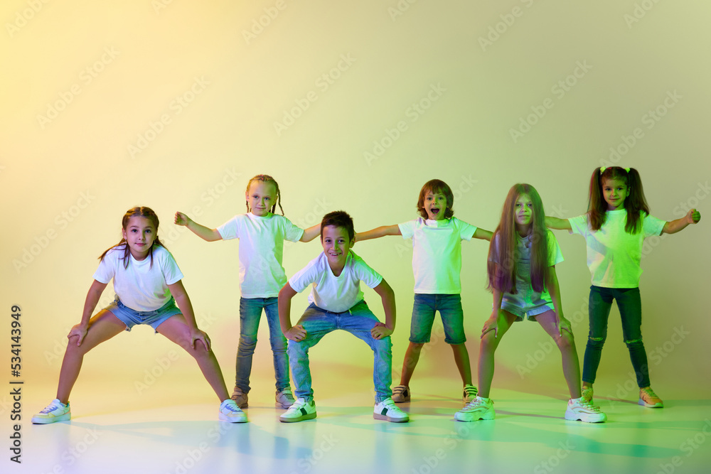 Fototapeta premium Group of children, active kids in sportive casual style clothes dancing in choreography class isolated on green background in yellow neon light.