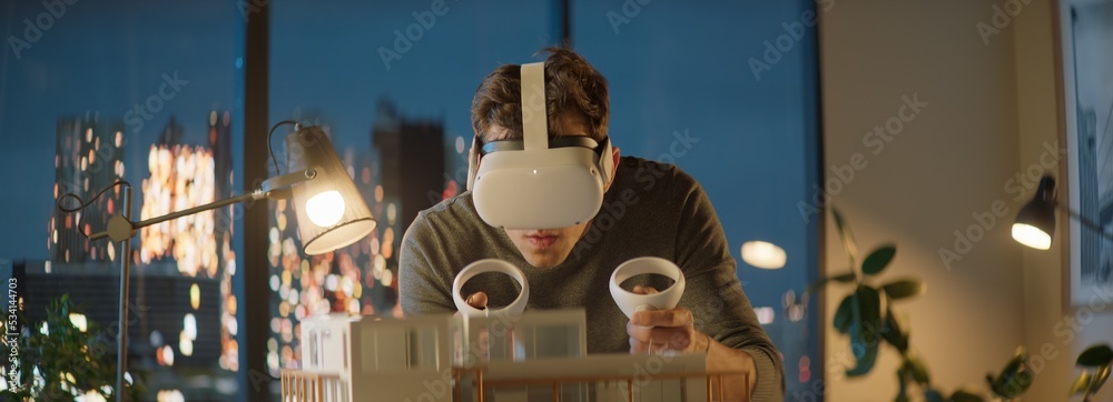 Portait of Caucasian male architect or student using a virtual reality VR  headset to work on a house project late at night, preparing for  presentation with a client foto de Stock