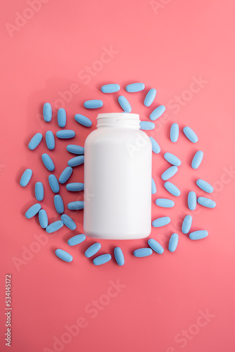 White plastic bottle with blue pills, vitamins or food supplemets. Blank container with medication pills on pink background. photo