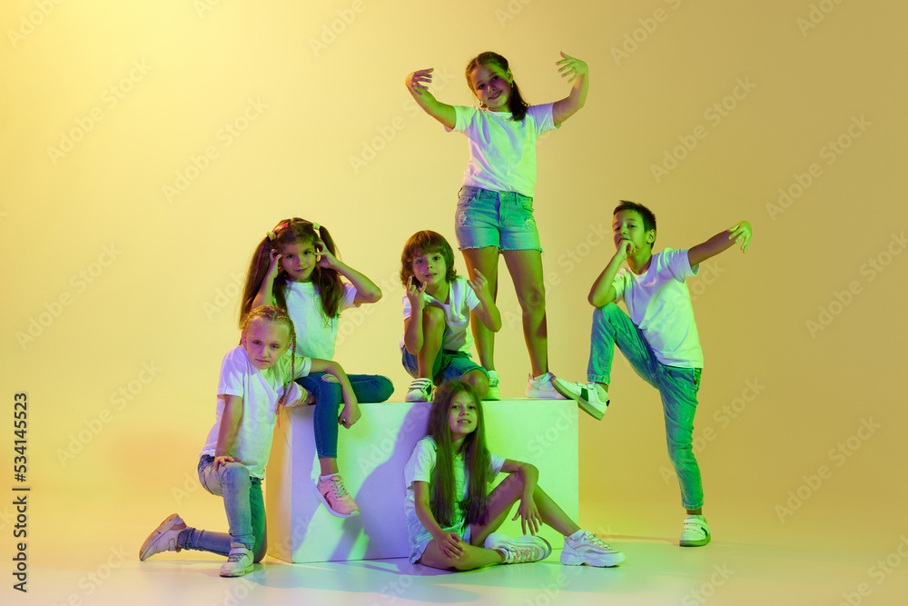 Obraz premium Dance class. Joyful children, kids in t-shirts and jeans dancing in action isolated on green background in yellow neon light.