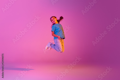Beautiful active little girl, kid jumping, dancing isolated over pink background in neon. Action, dance, happy childhood © master1305