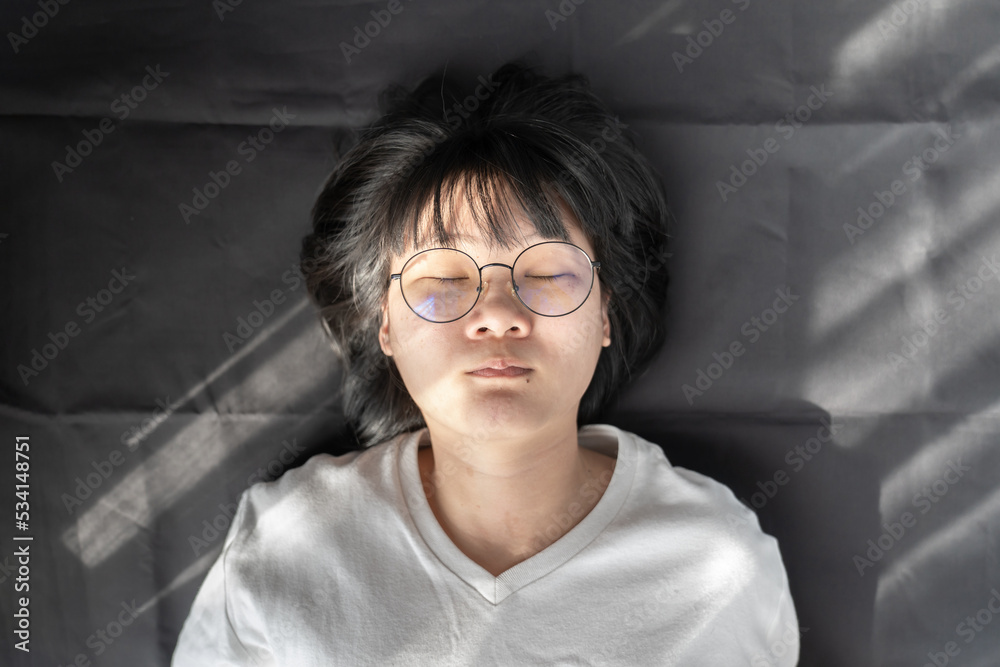 Cute short hair - glasses Asian woman laid on black wrinkled cloth background with window light on her. Cute short hair - glasses Asian woman laid on black wrinkled cloth background with window light on her.
