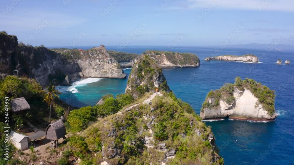 Distant aerial view of a person walking along the top of a cliff on the tropical island of Nusa Penida, Indonesia. Distant aerial view of a person walking along the top of a cliff on the tropical island of Nusa Penida, Indonesia.