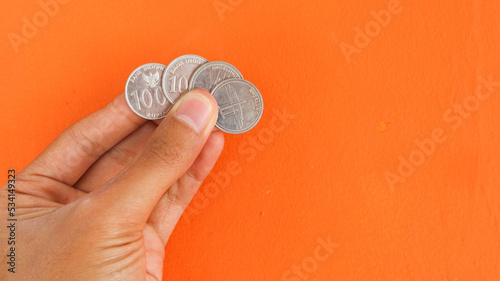 One thousand rupiah coin, hand holding of thousand rupiah coin isolated on an orange background. Indonesian rupiah currency