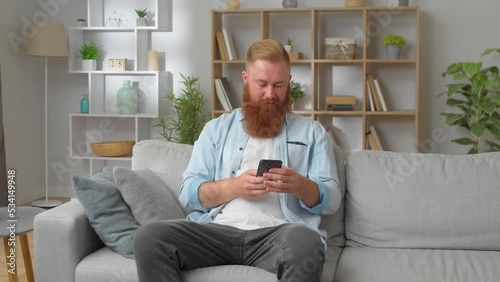 Satisfied smiling redhead man sit on sofa using cellphone device