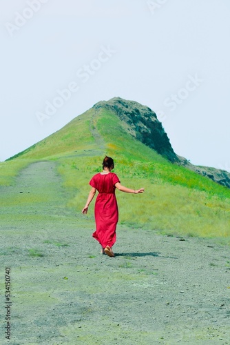 woman with long red dress walking on green mountain