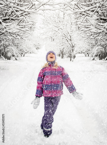 A girl child throws up snow on a snowy street.