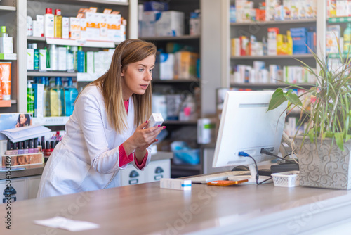 Pharmacist making prescription record through computer in pharmacy. Portrait of female pharmacist working with computer behind counter in pharmacy