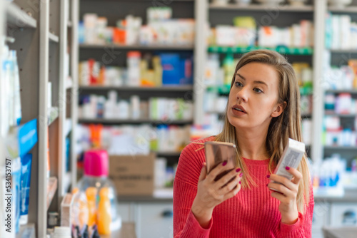 Profile shot of beautiful young woman shopping at pharmacy. Woman holding medication container while talking on cell phone. Woman holding medication box and dialing on cell phone