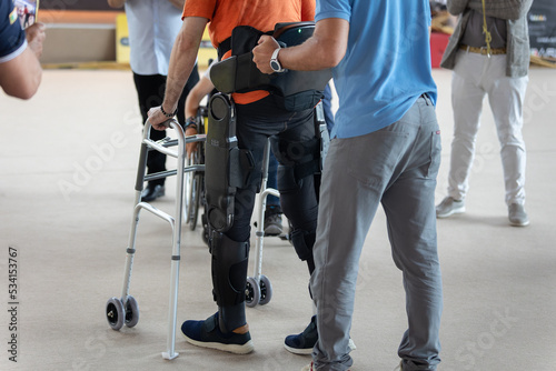 Boy with Mobility Problems in Lower Limbs in Upright Posture Walking Thanks to a Mechanical Exoskeleton and with the Help of his Physical Therapist