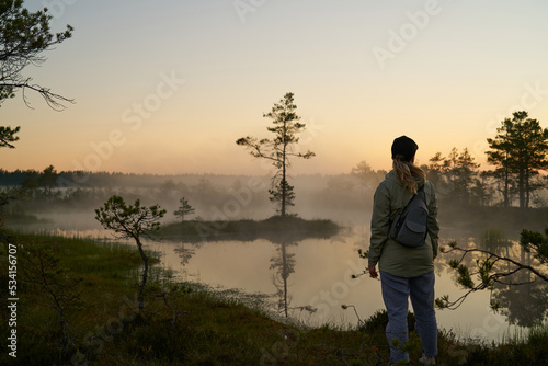 woman tourist meets dawn in nature. Sunset,  light and fog, Reflections of trees in lakes . Travel romance. Viru swamps Estonia.