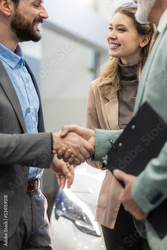 Young couple looking to buy a new car. Car salesman making a sale. Signing a papers for purchase a new car © Panorama