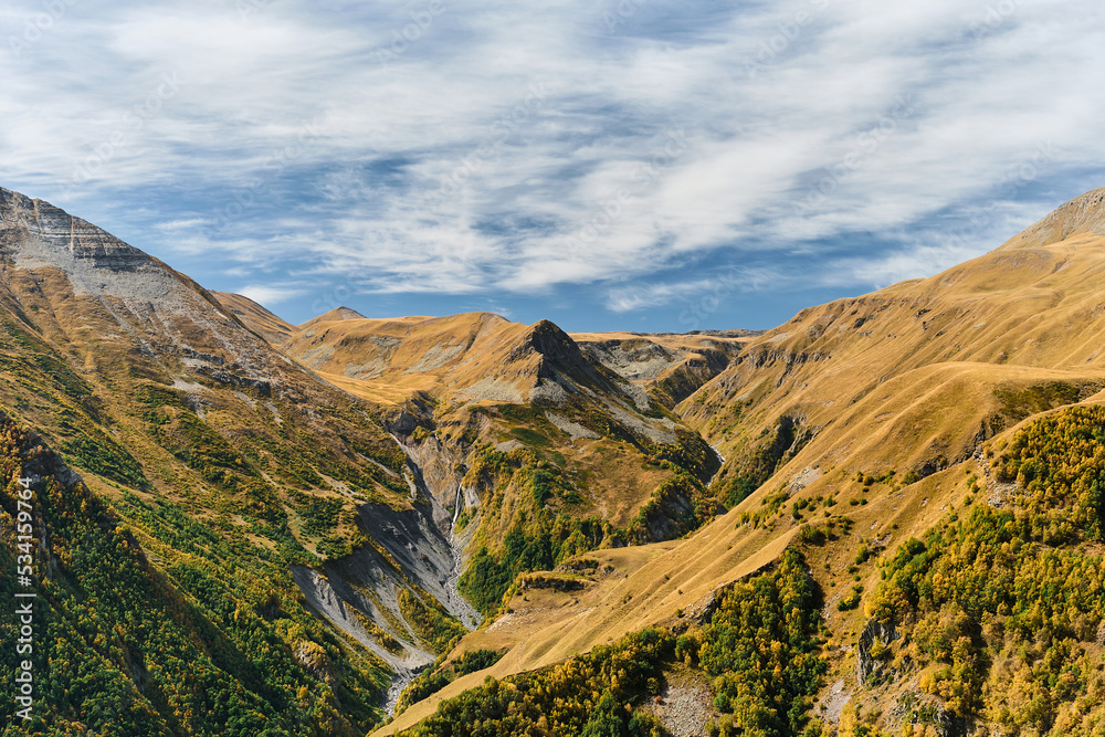 View of the gorge with a waterfall from the mountain plateau, autumn in the mountains. Idea for a banner or postcard with space for text, travel to Georgia, trekking in the mountains