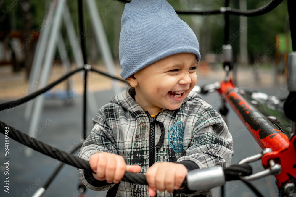 A kid in a gray plaid jacket is playing on a children's playground. The concept of a happy childhood A kid in a gray plaid jacket is playing on a children's playground. The concept of a happy childhood