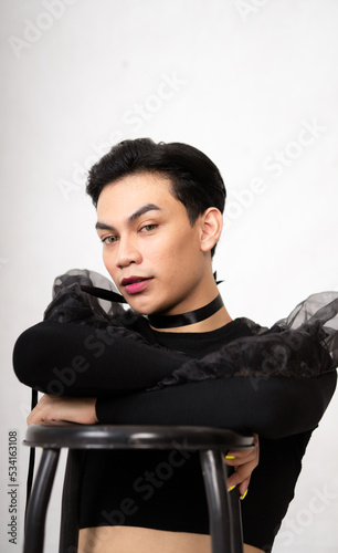 beautiful Asian man posing with the chair while wearing a black costume and makeup photo