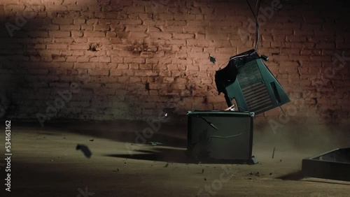 an old tube TV breaks on a concrete floor against a brick wall